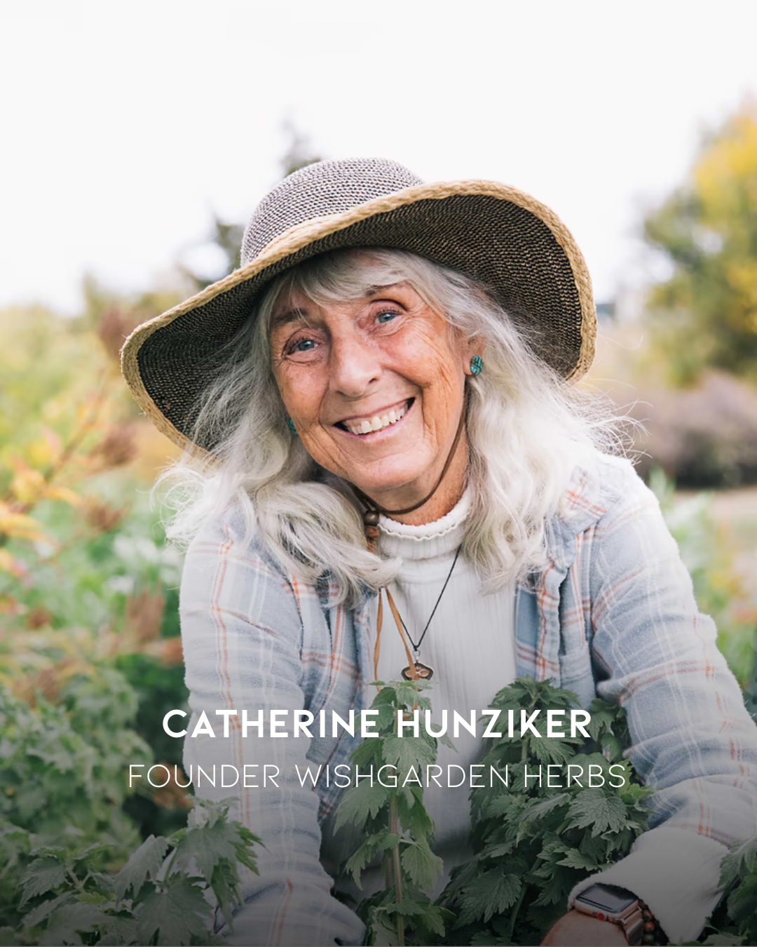 Woman with gray hair and a wide-brimmed hat standing among plants, identified as the founder of Wishgarden Herbs.